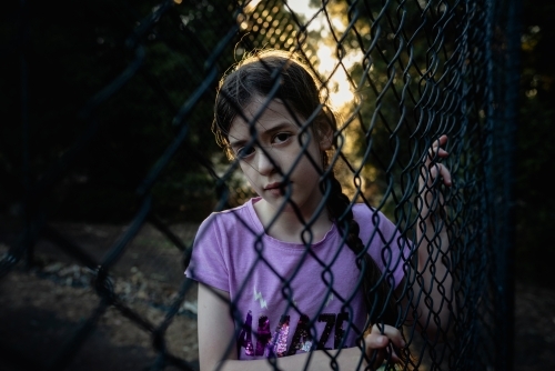 Portrait of a serious, young girl looking through a wire fence - Australian Stock Image
