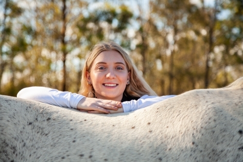 Portrait of a smiling blonde teen resting on her horse - Australian Stock Image