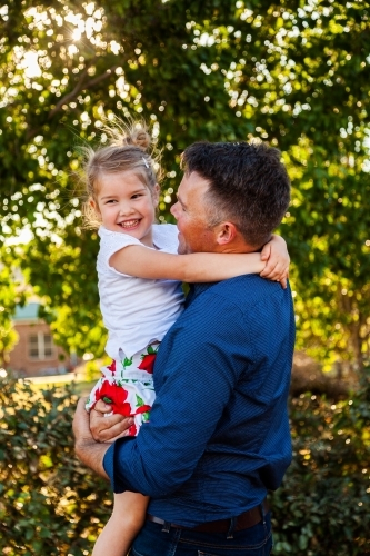 Portrait of a smiling father hugging his happy daughter in golden sunlight - Australian Stock Image