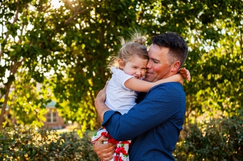 Portrait of a smiling father hugging his happy daughter in golden sunlight