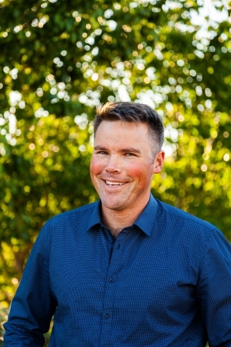 Portrait of a smiling man with bokeh green background - Australian Stock Image
