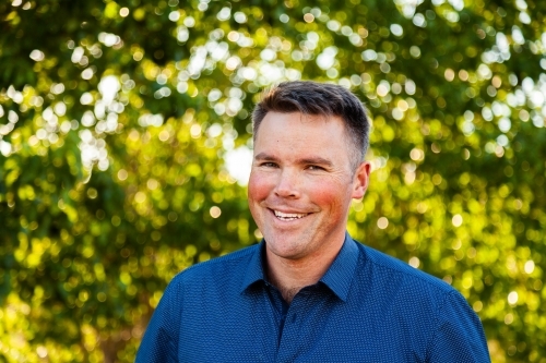 Portrait of a smiling man with bokeh green background - Australian Stock Image