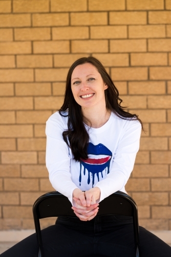 Portrait of a smiling woman with long dark hair, sitting astride a chair clasped hands - Australian Stock Image