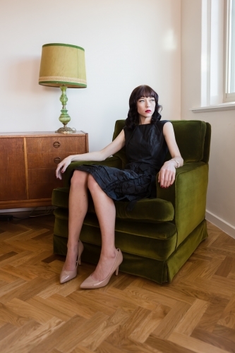 Portrait of a woman in a beautiful dress sitting in a green velvet armchair - Australian Stock Image