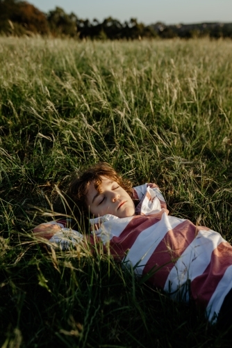 Portrait of a young boy lying with his hands behind his head in a tall grass field at sunset