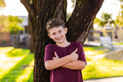 portrait of a young confident aussie 9yo boy leaning against tree - Australian Stock Image
