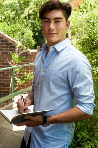 Portrait of a young male outdoors with a notebook - Australian Stock Image