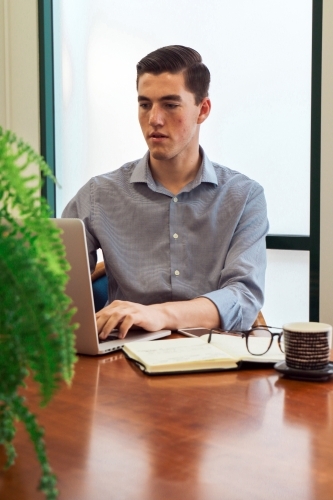 Portrait of a young office worker sitting with laptop and note book at a meeting table