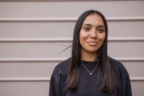 Portrait of a young, smiling,  first nations woman against wall outside - Australian Stock Image