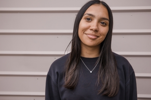 Portrait of a young, smiling,  first nations woman against wall outside - Australian Stock Image