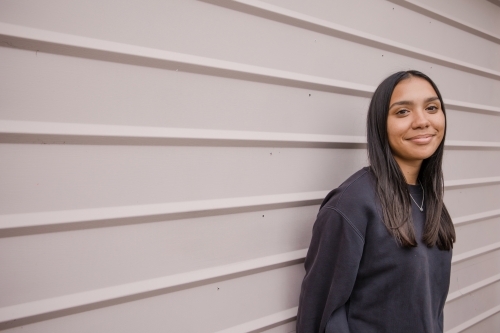 Portrait of a young, smiling,  first nations woman against wall outside - Australian Stock Image