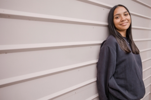 Portrait of a young, smiling,  first nations woman against wall outside - Australian Stock Image