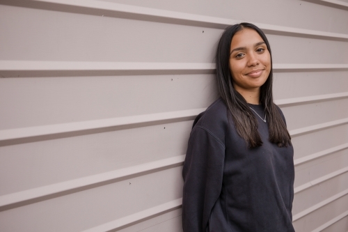 Portrait of a young, smiling,  first nations woman against wall outside - Australian Stock Image