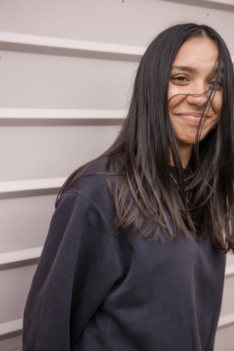 Portrait of a young, smiling, first nations woman against wall outside - Australian Stock Image