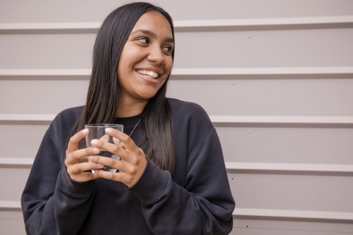 Portrait of a young, smiling, first nations woman holding a glass of water - Australian Stock Image