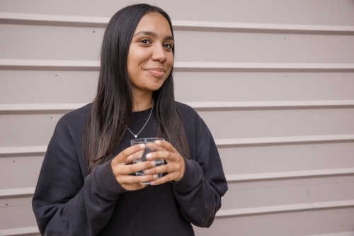 Portrait of a young, smiling, first nations woman holding  a glass of water - Australian Stock Image