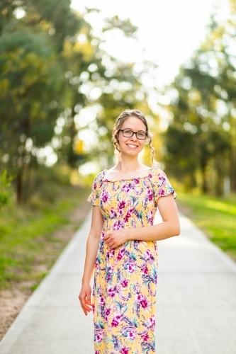 Portrait of a young woman with glasses standing on a pedestrian foot path through a park - Australian Stock Image