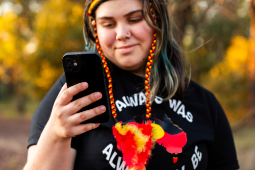 Portrait of Aboriginal Australian teenaged girl using mobile phone device focus on smartphone - Australian Stock Image
