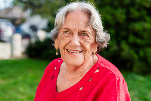 Portrait of an elderly woman sitting on wooden bench outdoors smiling - Australian Stock Image