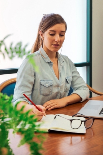 Portrait of an office worker sitting with laptop and note book at a meeting table - Australian Stock Image