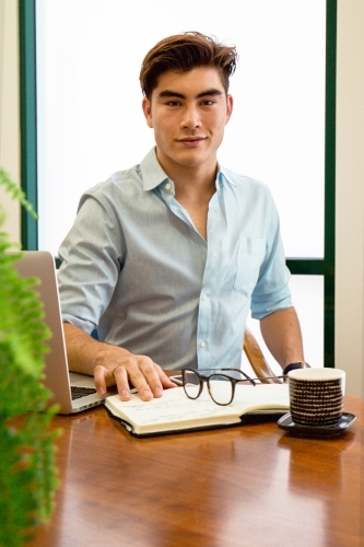 Portrait of an office worker sitting with laptop and note book at a meeting table - Australian Stock Image