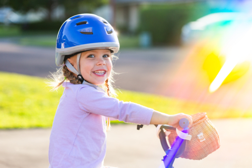 Portrait of Australian child and rainbow light over girl riding bike in blue helmet - Australian Stock Image