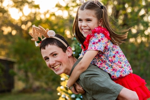 Portrait of brother giving sister piggyback ride outside at Christmas time in Australia - Australian Stock Image