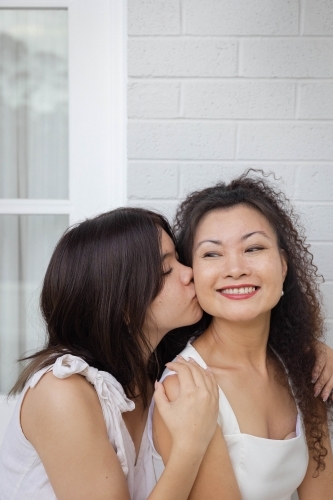 Portrait of daughter kissing mother on the cheek - Australian Stock Image