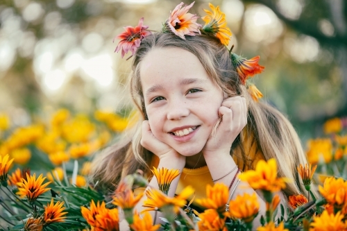 Portrait of girl lying in field with vibrant orange and yellow gazania wildflowers - Australian Stock Image