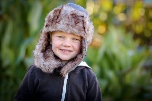 Portrait of happy 3 year old boy wearing warm hat outdoors on cold winter day - Australian Stock Image