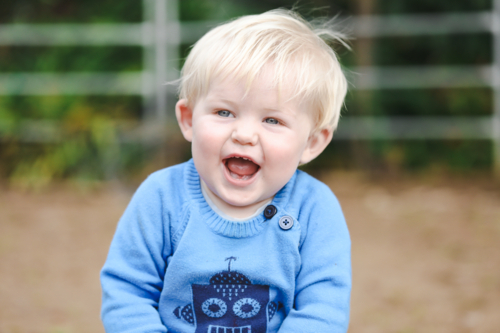 Portrait of happy little toddler boy sitting in garden smiling - Australian Stock Image