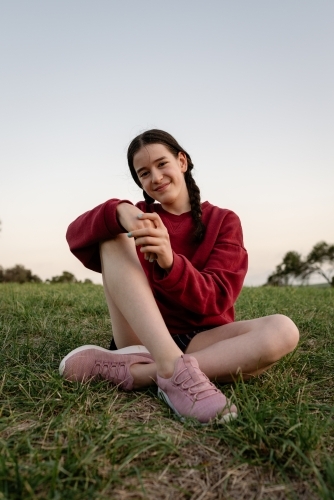 Portrait of happy young adolescent girl with braided hair sitting cross legged on grass