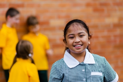 Portrait of happy young Aussie school girl of Filipino ethnicity smiling and wearing a dress - Australian Stock Image