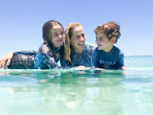 Portrait of Mother and two children in ocean leaning on surfboard