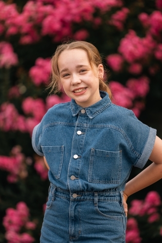 Portrait of pre-teen girl standing in front of vibrant pink bougainvillea bush - Australian Stock Image