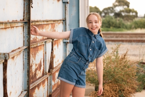 Portrait of pre-teen girl wearing denim jump suit in front of large blue barn door - Australian Stock Image