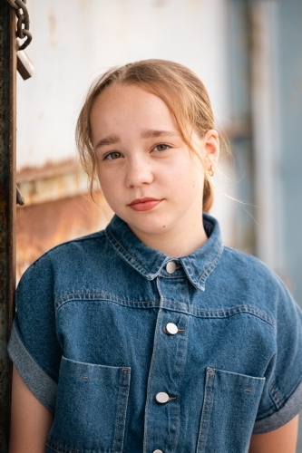 Portrait of pre-teen girl wearing denim jump suit in front of large blue barn door