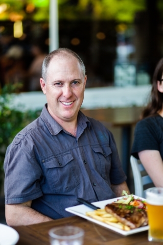 Portrait of smiling middle aged man sitting at cafe - Australian Stock Image
