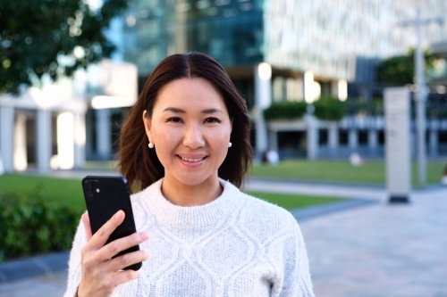 Portrait of smiling woman holding phone next to park