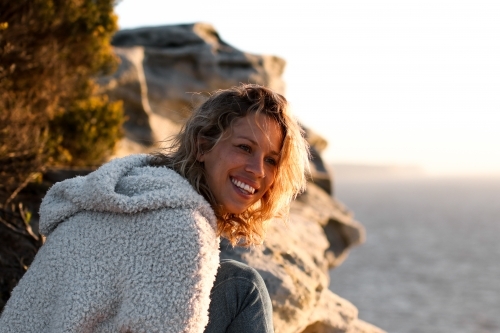 Portrait of smiling young woman on coastal clifftop at sunrise - Australian Stock Image