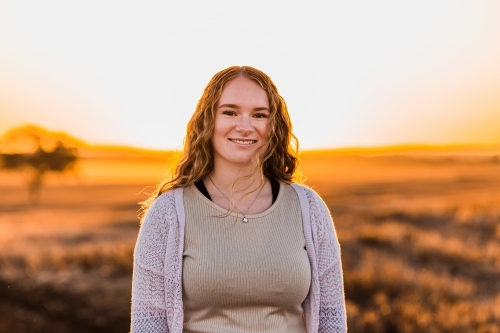 Portrait of teenage girl smiling against sunset rural landscape - Australian Stock Image