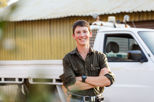 Portrait of teenaged young man standing with his first car a ute by shed on a rural property - Australian Stock Image