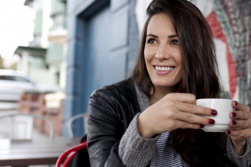 Portrait of woman sitting at a cafe smiling and holding a cup