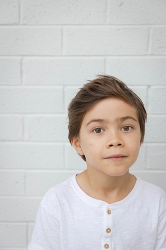 Portrait of young boy against white wall - Australian Stock Image