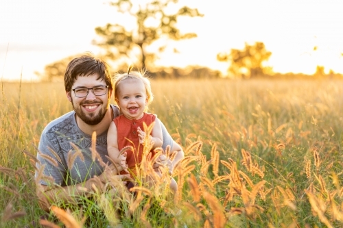 Portrait of young father in his early twenties with baby girl in long grass on Australian farm - Australian Stock Image