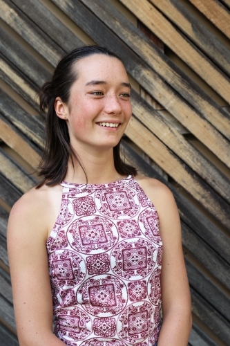 Portrait of young female smiling in front of textured wooden panelling - Australian Stock Image