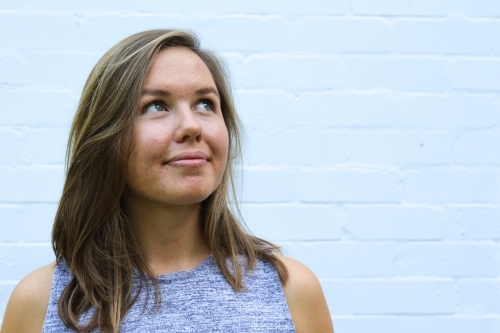 Portrait of young girl smiling in front of white brick wall - Australian Stock Image