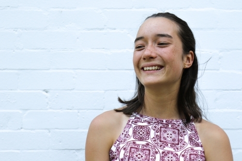 Portrait of young girl smiling in front of white brick wall - Australian Stock Image