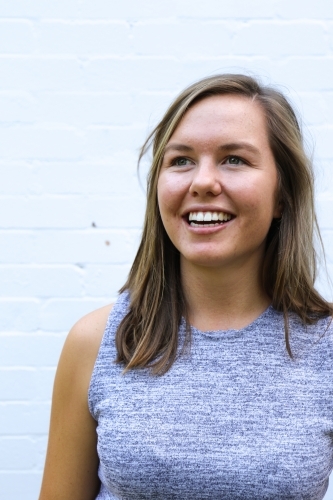 Portrait of young girl smiling in front of white brick wall - Australian Stock Image