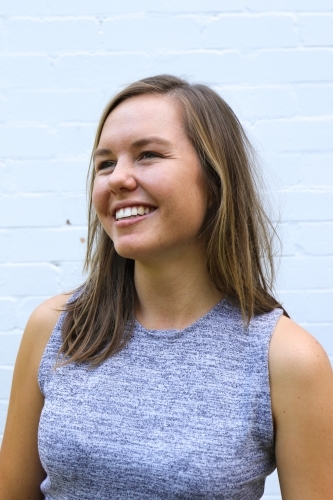Portrait of young girl smiling in front of white brick wall - Australian Stock Image